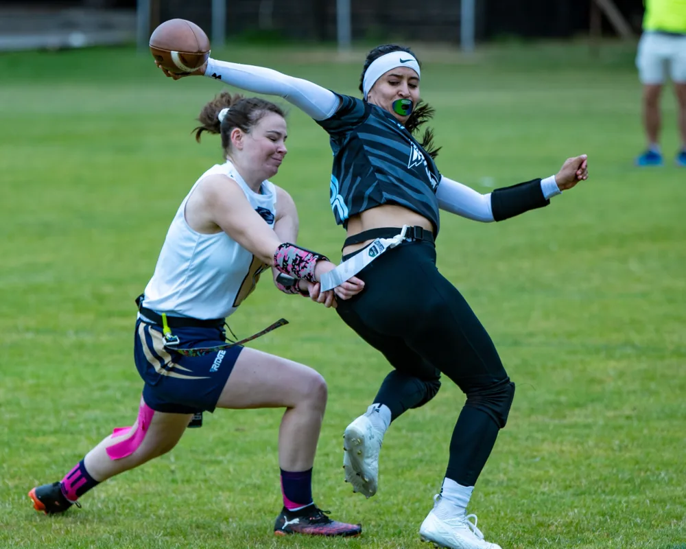 A flag football quarterback releases a pass as a defender reaches towards her waist flag.