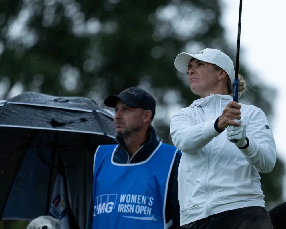 Golfer following through on swing beside caddie