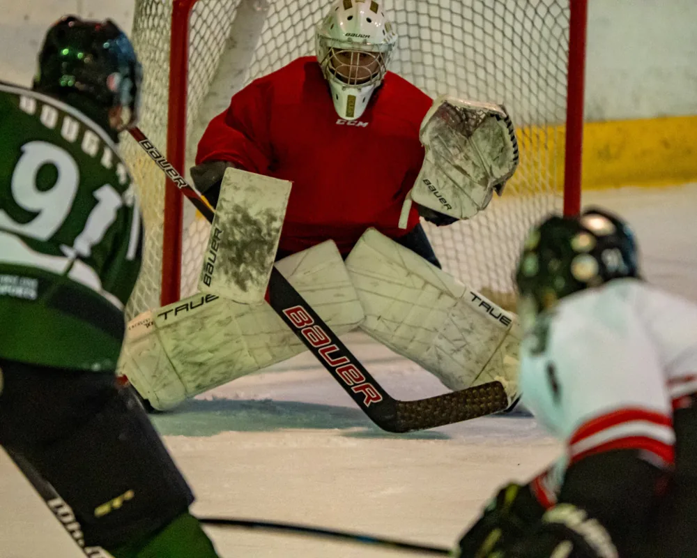 A goaltender in red guards the net as players converge in front.