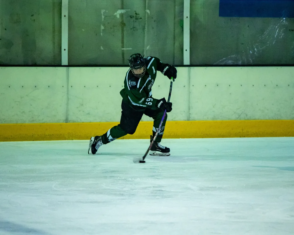 A Belfast Grizzlies player in green skates with the puck near the boards.