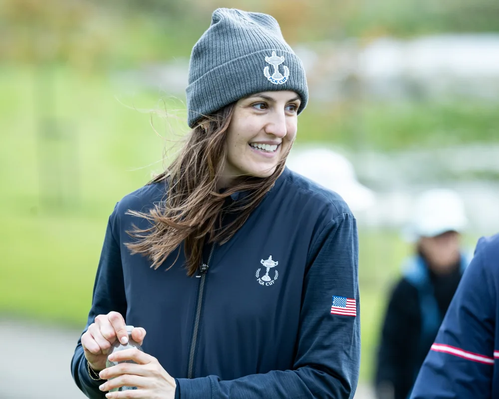 A smiling Team USA golfer in a grey beanie clasps their hands.
