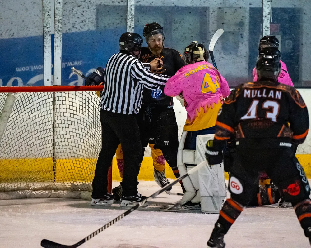 Referee stands between players near the goal