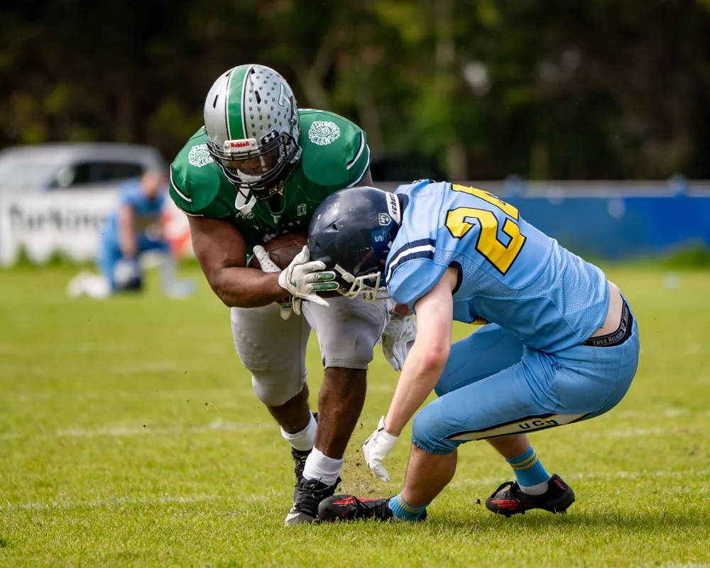 A Belfast Trojans ball carrier braces as a UCD defender reaches to tackle him.