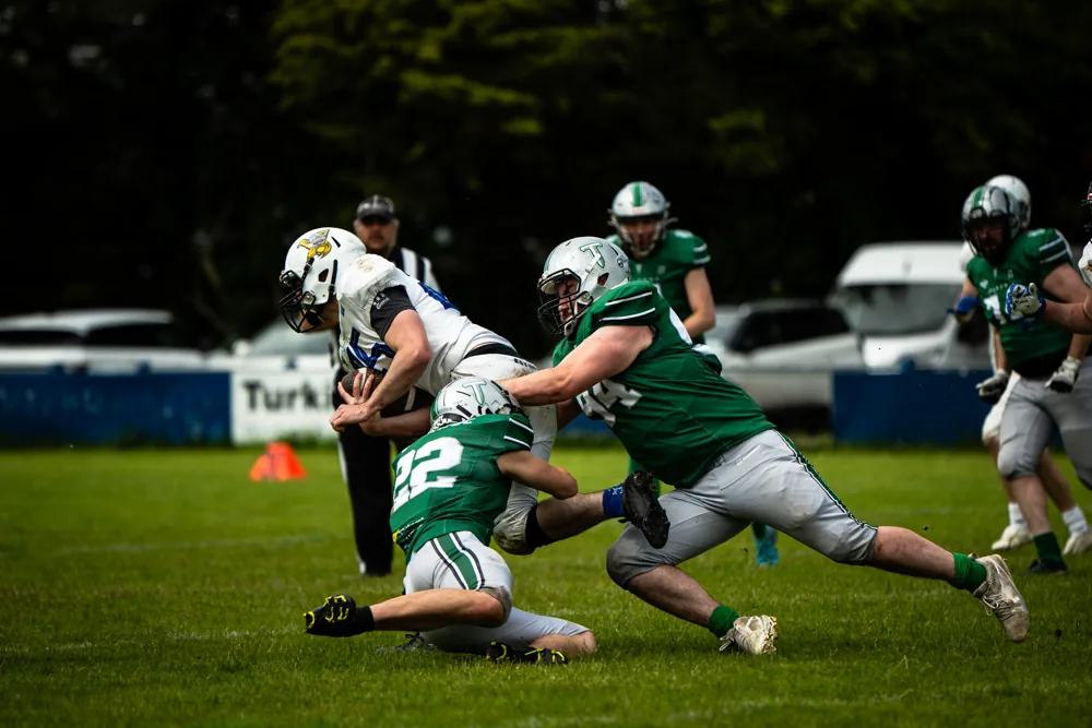 Two Belfast Trojans defenders tackle a UL Vikings ball carrier in white.
